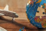 Incomplete Earth globe puzzle near medical face masks and airplane model on wooden background. 